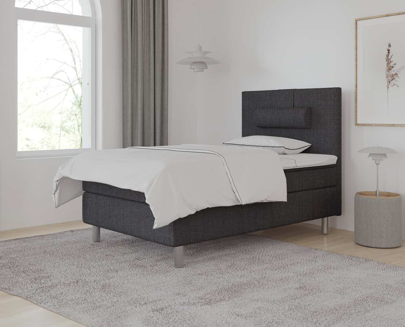 Eksklusivt lavet seng med skræddersyet sengeramme i mørk stof, der kombinerer moderne komfort med elegant design. Perfekt til at skabe et stilfuldt soveværelse.